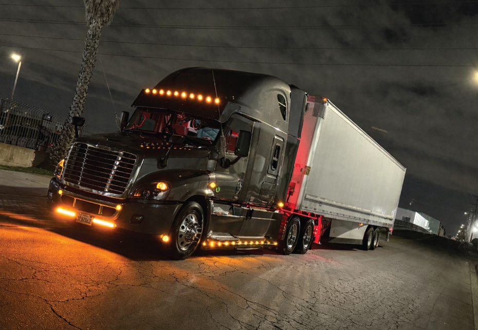 Image of an 18 wheeler at night with lights on.